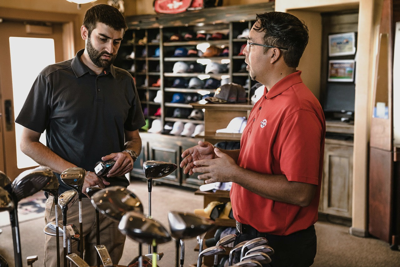 Golf club staff assisting a golfer with club preparation in a pro shop, illustrating seamless golf club shipping and coordination with BagCaddie.